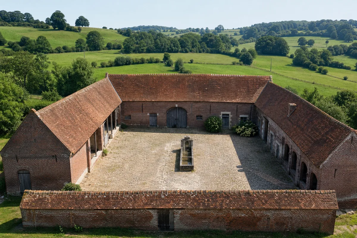 Corps de ferme en brique rouge du Hainaut avec cour pavée sous un ciel clair