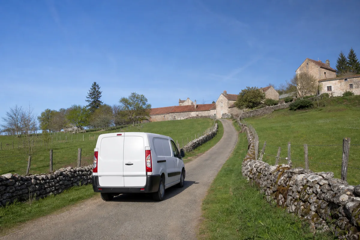 Route de coteau menant à un hameau du Bugey sud avec maisons en pierre et fourgon utilitaire